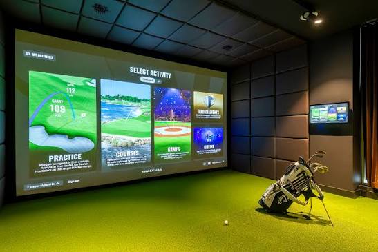 Golf simulator room with a full-height projection screen, artificial turf and a Callaway bag on the hitting mat