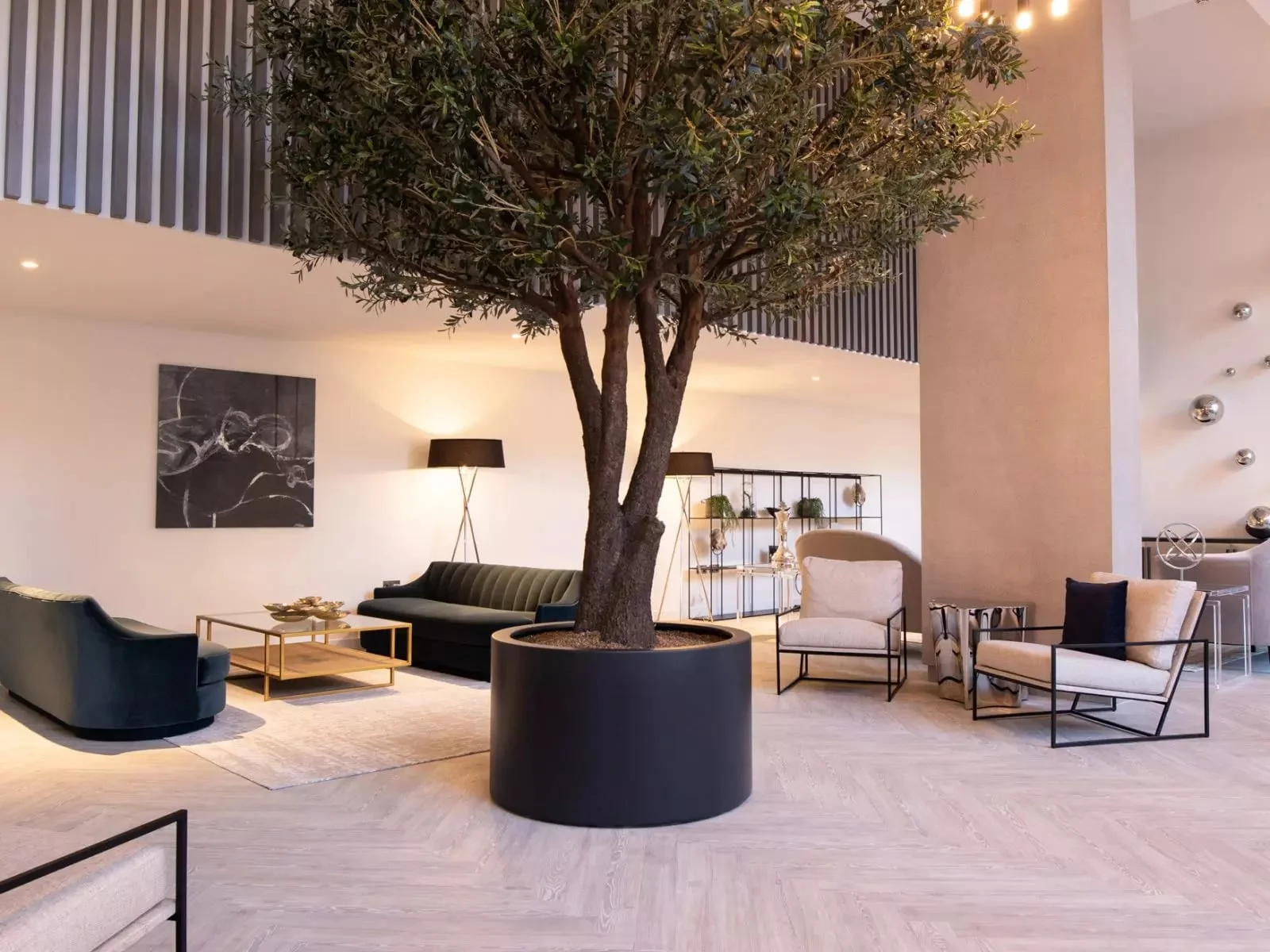 Double-height residents’ lounge with an olive tree, velvet sofas and lounge seating