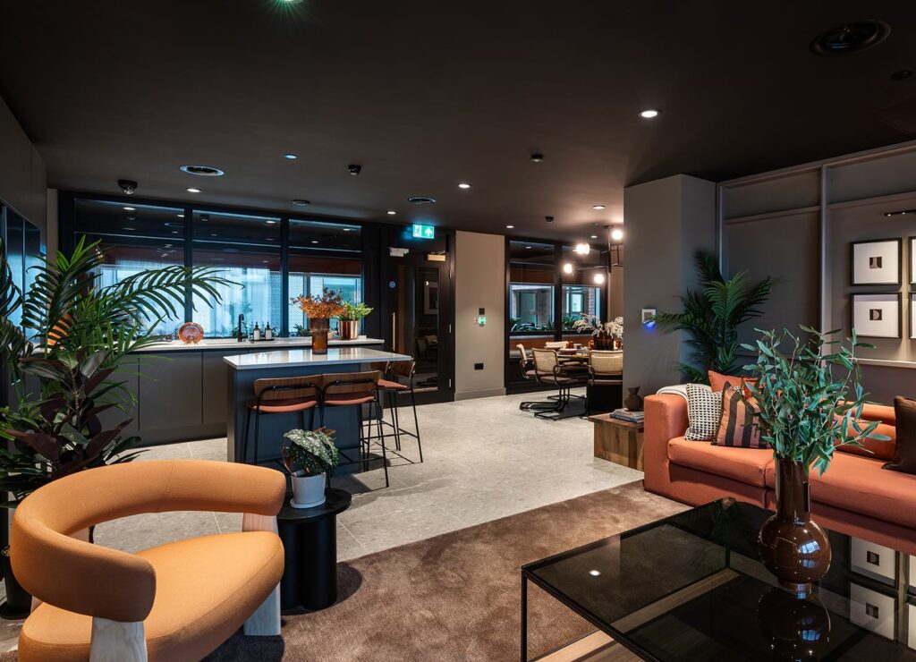 Residents’ lounge with an orange sofa, a kitchen bar with stools and dining tables beyond