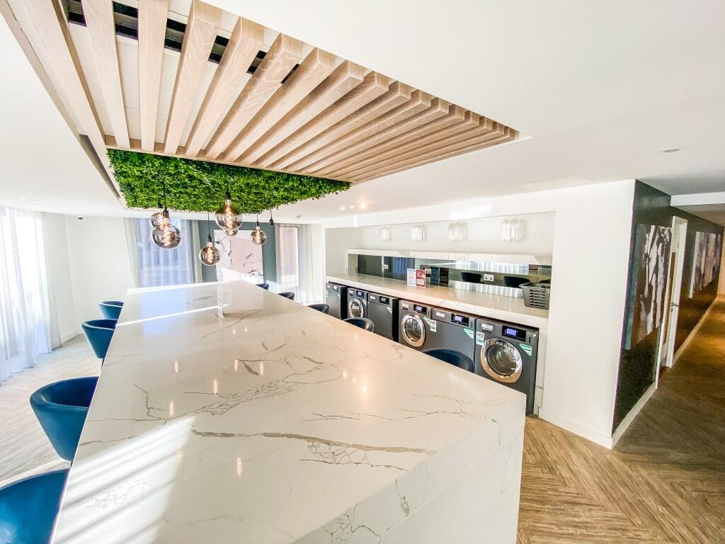 Residents’ kitchen with a marble island, bar seating and a laundry room with washing machines beyond