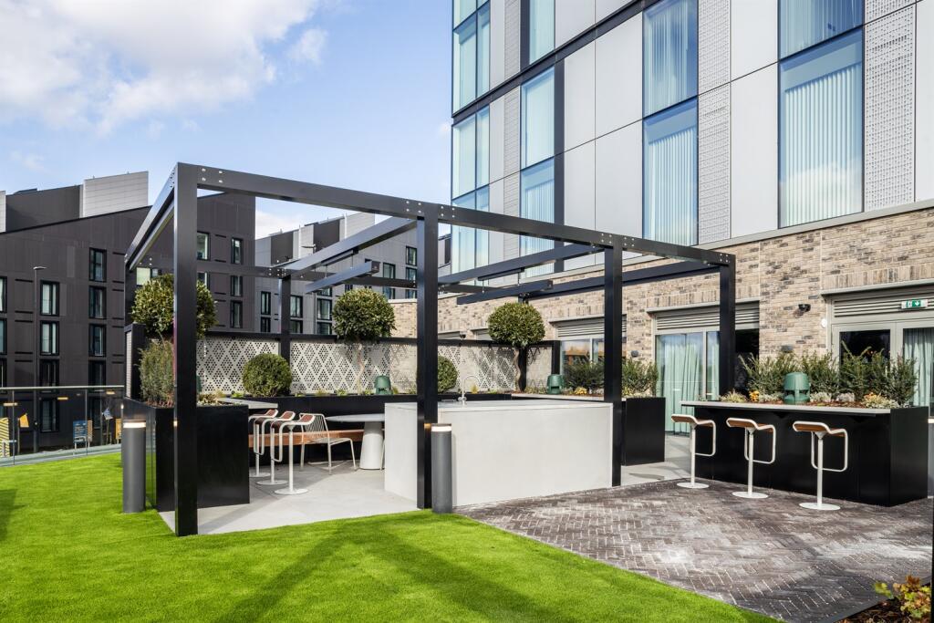 Terrace with artificial grass, a brick-paved patio, a black steel pergola, an outdoor counter with stools and a dining table