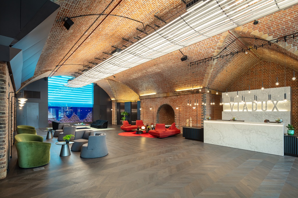 Reception lobby beneath a brick vaulted ceiling with a marble reception desk, lounge seating and illuminated Viadux lettering