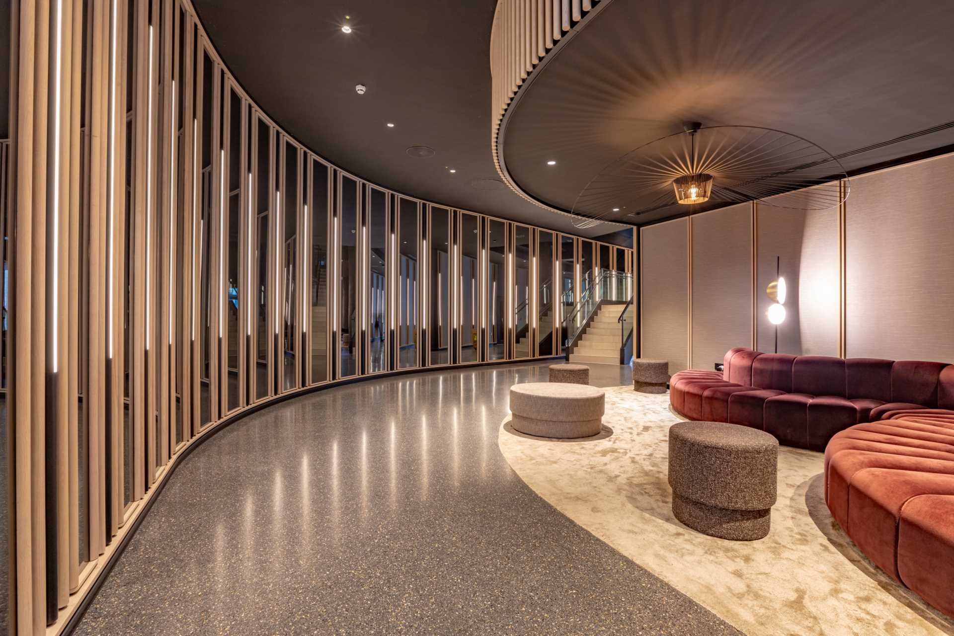 Lounge with a curved sofa and poufs against a slatted timber wall with integrated lighting