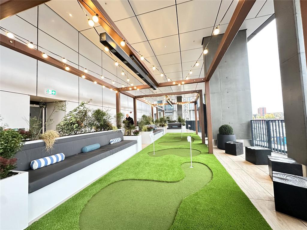 Covered terrace with the putting course and white flag pins, cushioned benches, planter boxes and a festoon-lit pergola