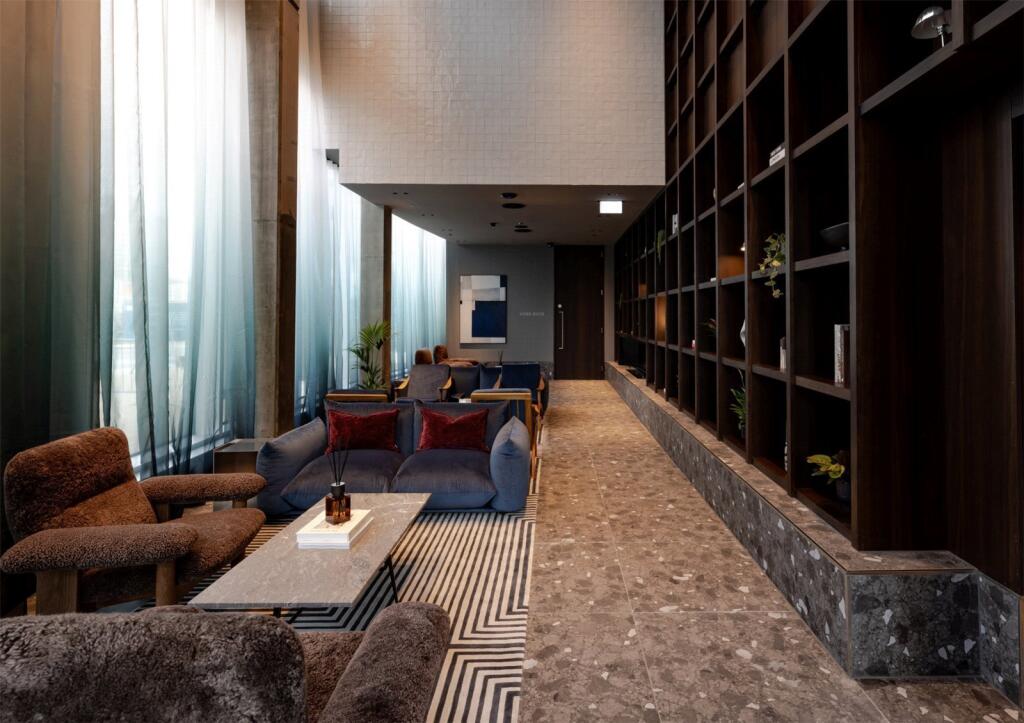 Double-height lounge with floor-to-ceiling shelving, a blue sofa, brown armchairs and tall curtained windows; a Board Room door sign is visible in the hallway