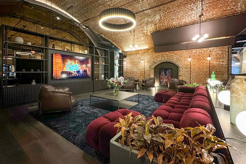 Lounge beneath a brick vaulted ceiling with a circular ring light, sofas, armchairs and a wall-mounted screen