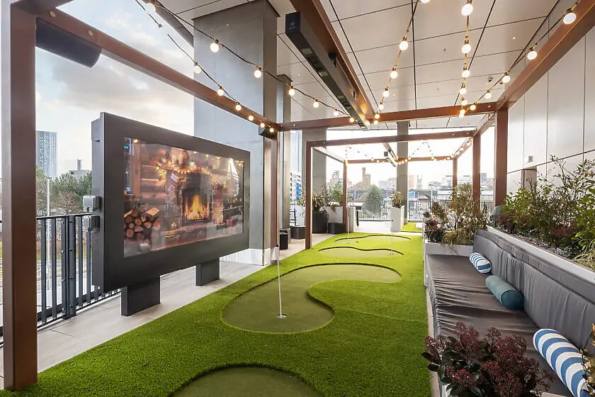 Covered terrace with a mini-golf putting green, a large outdoor screen showing a fireplace, a festoon-lit pergola and bench seating