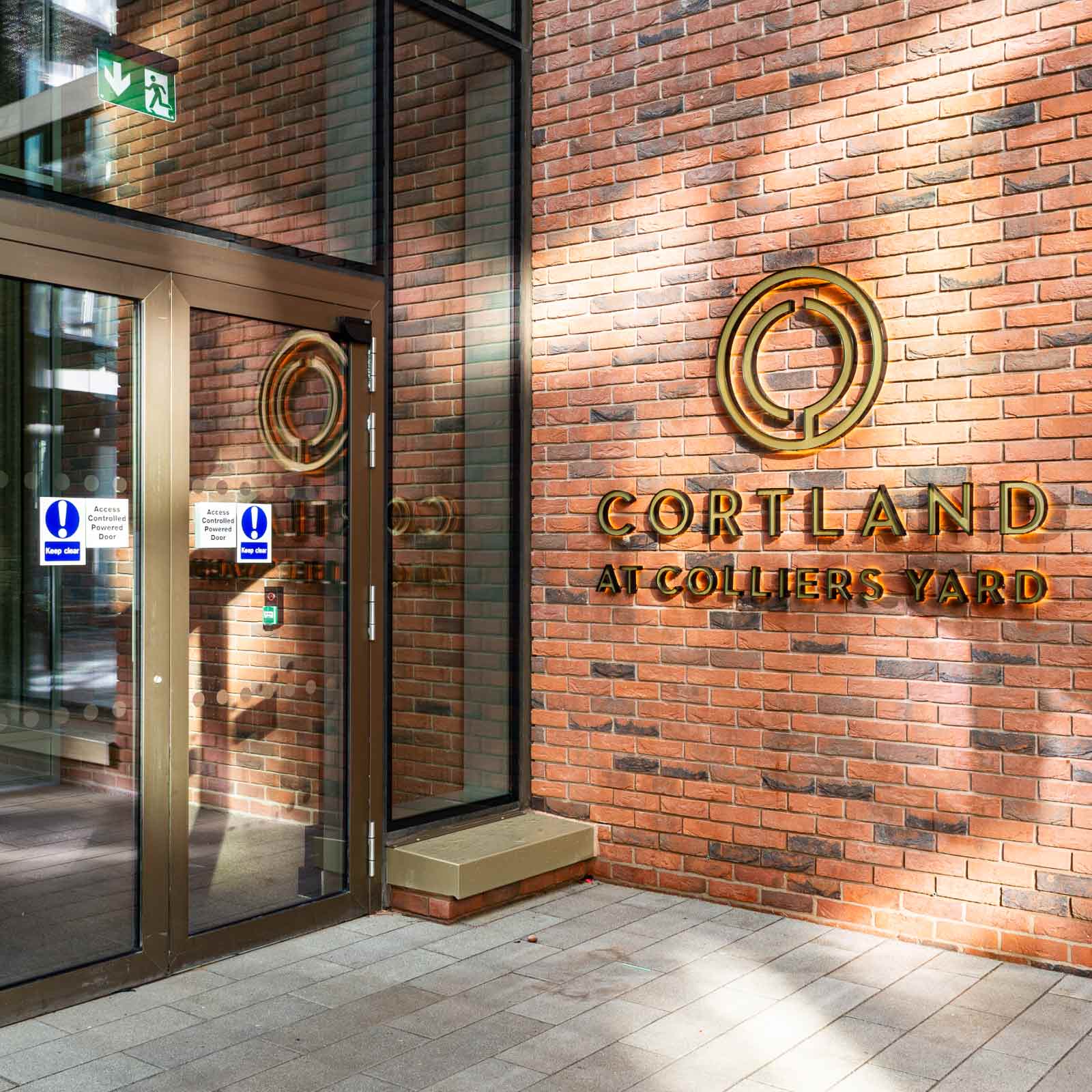 Street-level entrance with illuminated Cortland at Colliers Yard lettering on brick
