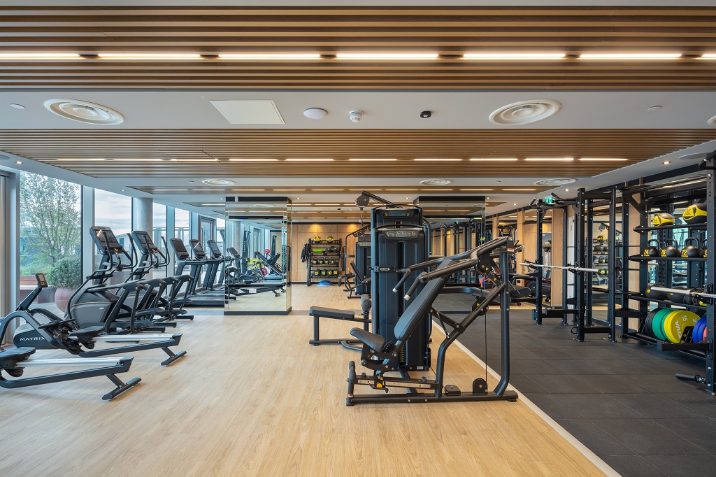 Gym with rowing machines, treadmills and cross-trainers beside tall windows, with cable machines, squat racks and free weights