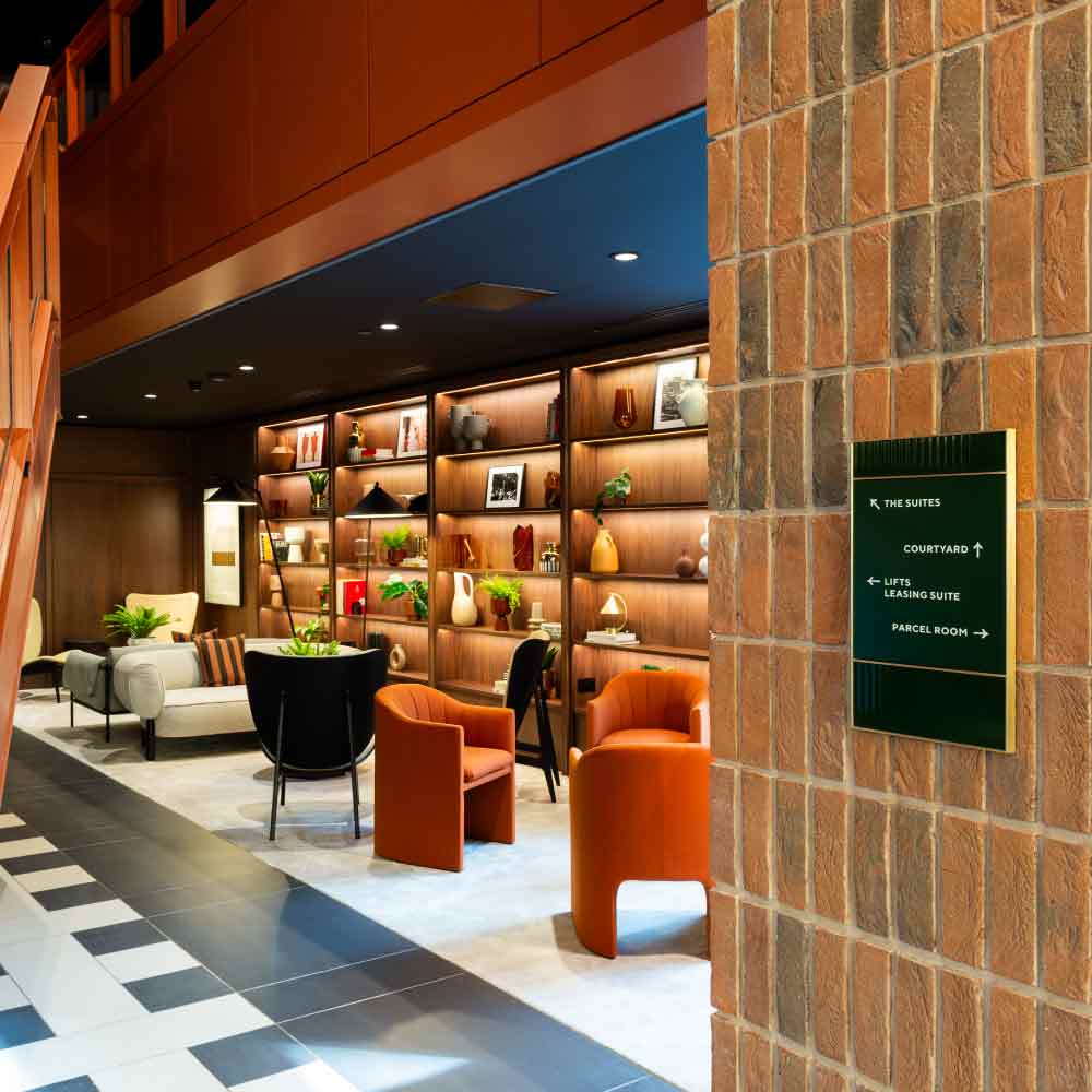 Residents’ lounge with display shelving and a signpost to The Suites, Courtyard, Leasing Suite and Parcel Room