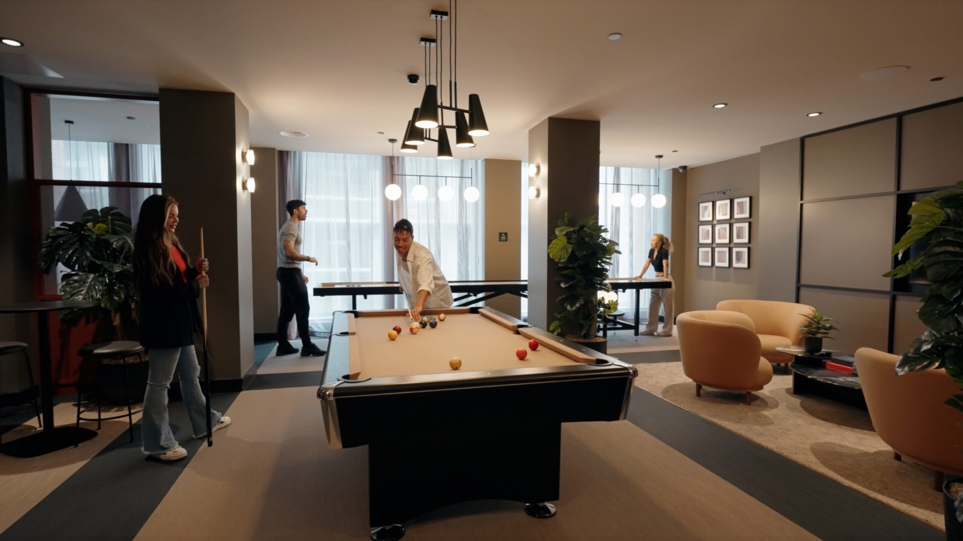 Games room with a pool table, a shuffleboard table, high-top tables and lounge seating by floor-to-ceiling windows