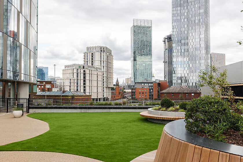 Roof terrace with artificial turf, timber planters and bench seating overlooking the city skyline